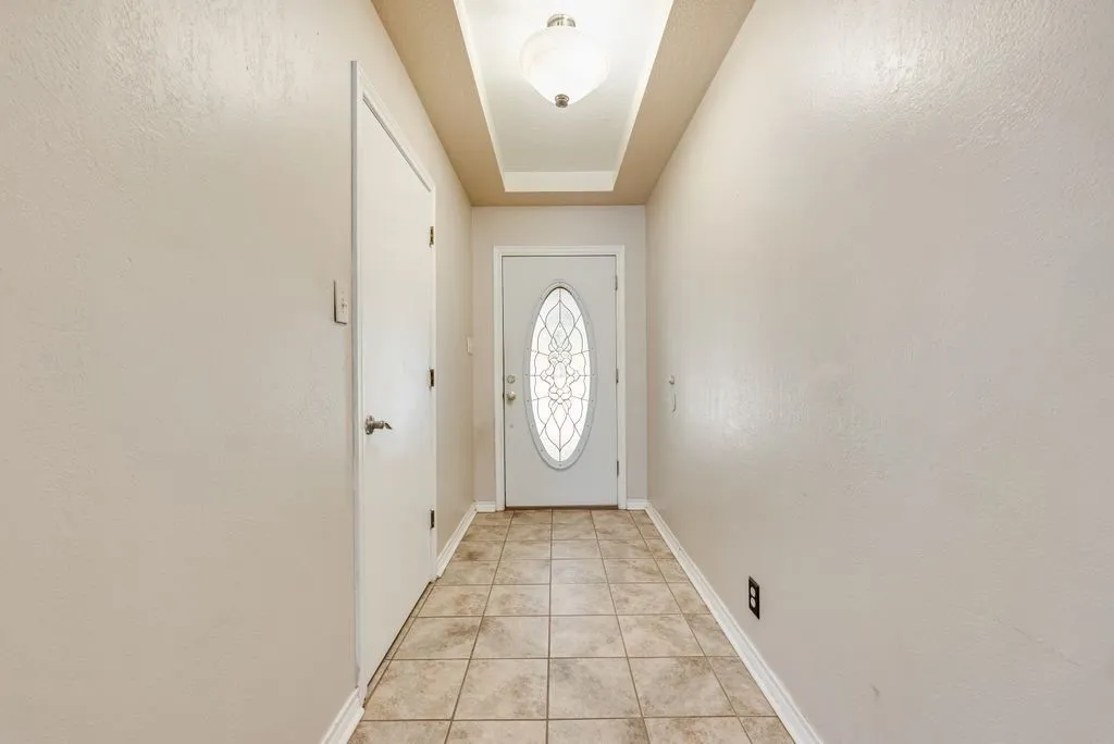 Tiled entryway featuring a decorative glass front door, recessed ceiling detail with a flush-mount light fixture, and neutral wall tones