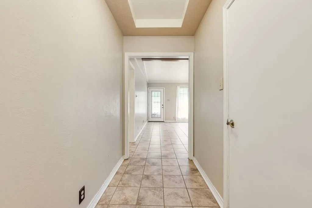 Hallway featuring neutral-toned walls, tile flooring, and a tray ceiling detail
