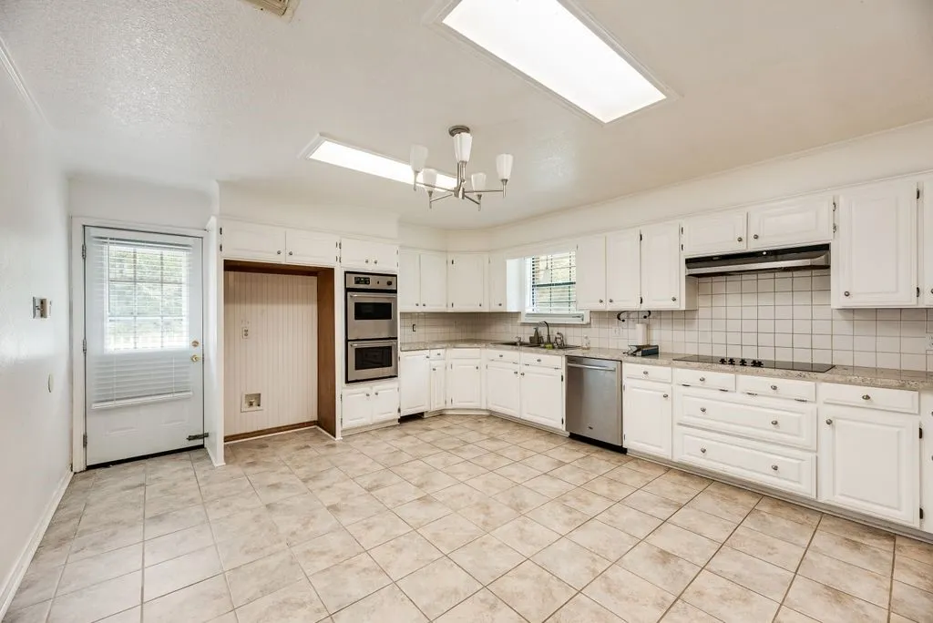 Kitchen featuring white cabinetry, tile flooring, built-in double ovens, a flat-top stove, and a stainless steel dishwasher