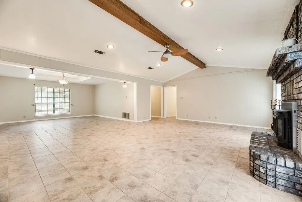 Spacious living area featuring neutral tile flooring, a vaulted ceiling with exposed wood beam, recessed lighting, and a brick fireplace