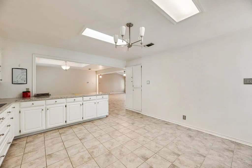 Spacious kitchen featuring white cabinetry, light-toned tiled flooring, and a large pass-through opening