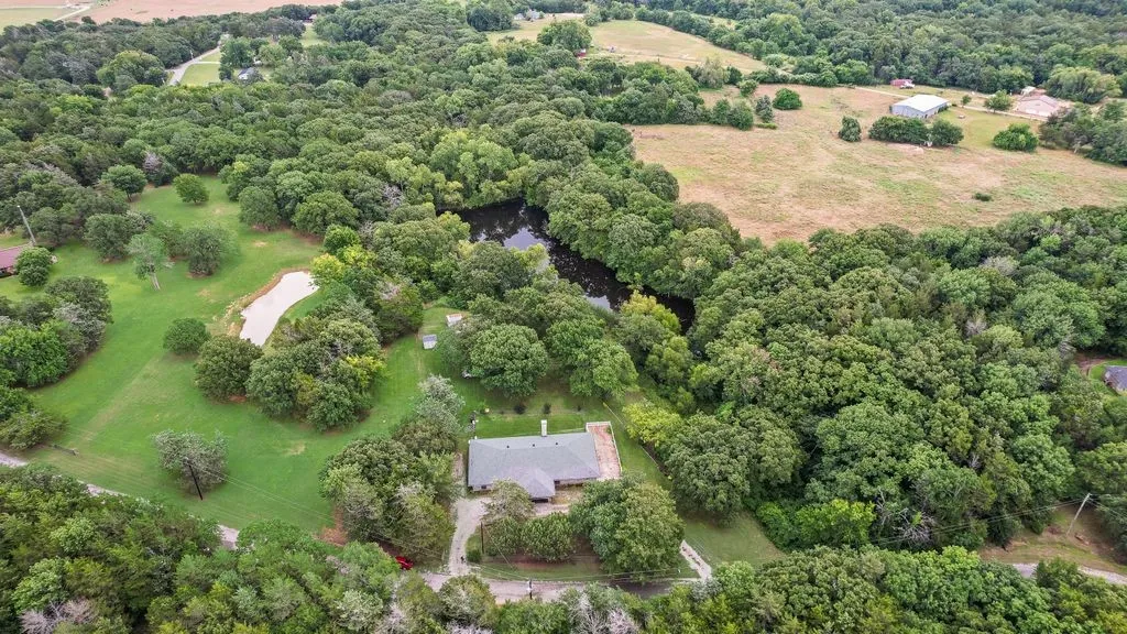 Expansive property featuring a single-story residence, a private pond, mature trees, a natural water feature, and open grassy areas