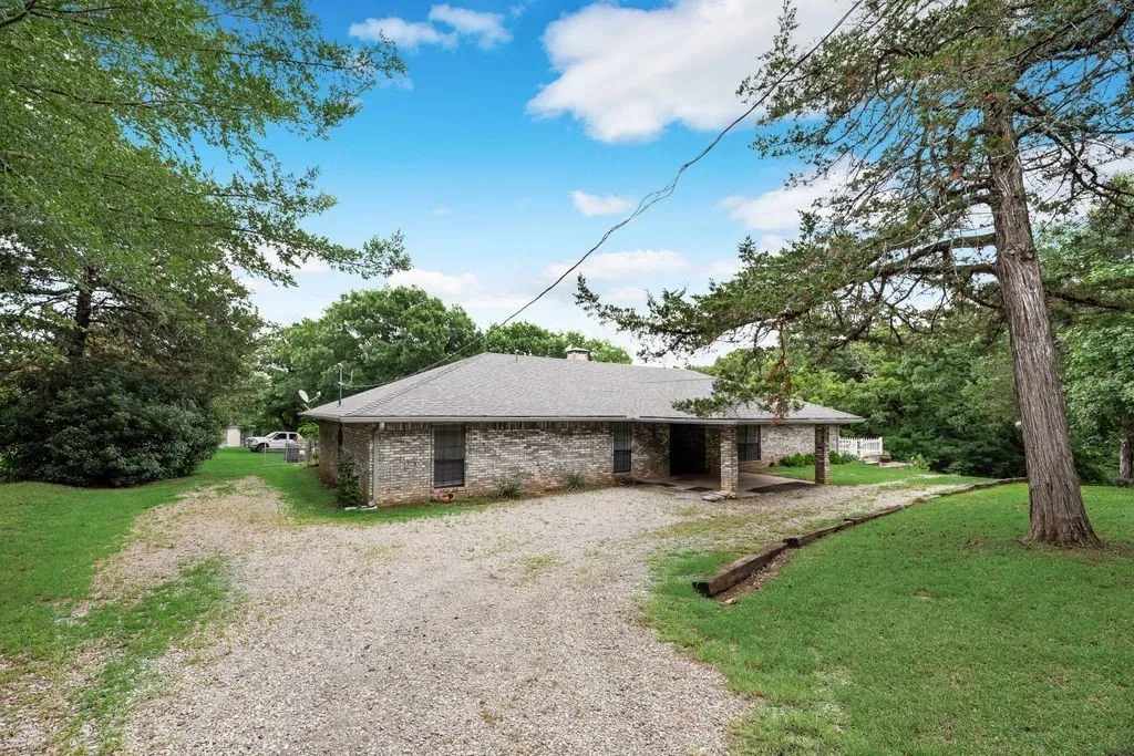 Brick exterior featuring a covered front entry with stone columns and a gravel driveway