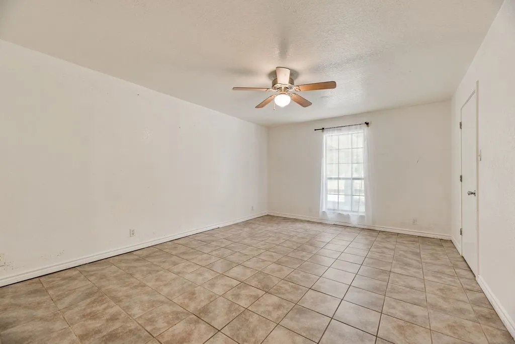 Spacious room featuring neutral-toned tile flooring, a window with natural light, and a ceiling fan with integrated lighting
