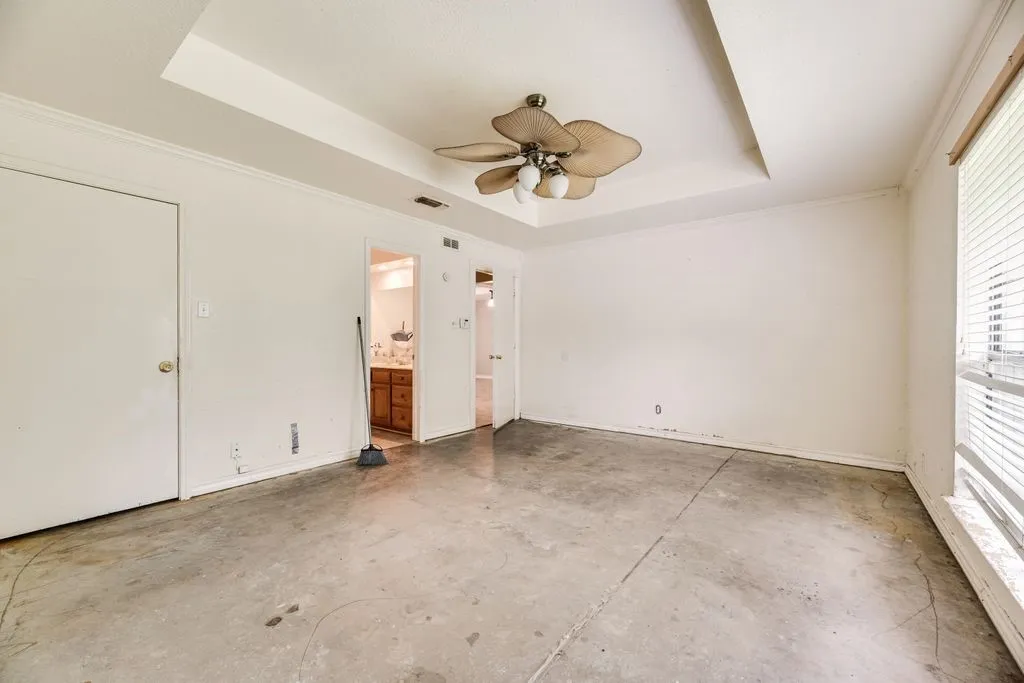 Spacious room featuring a tray ceiling with a ceiling fan, concrete flooring, and crown molding