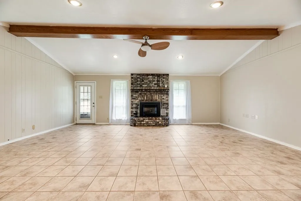Spacious living area featuring neutral-toned tile flooring, a prominent brick fireplace, and dual windows