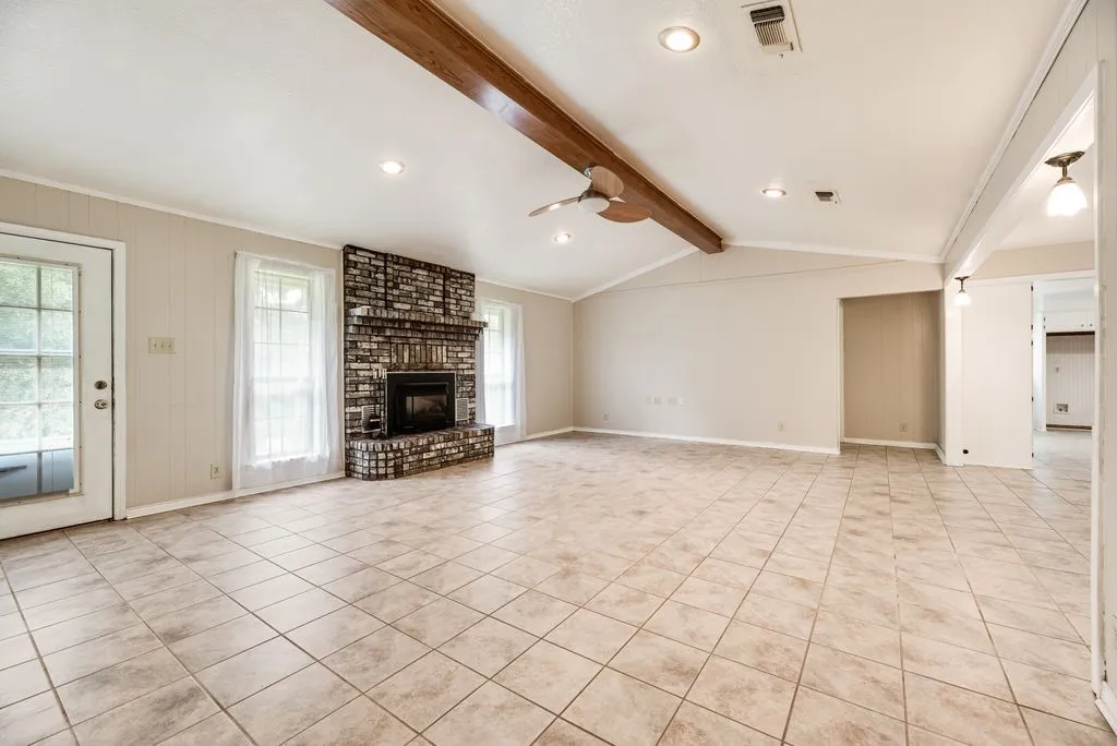 Spacious living area featuring a corner brick fireplace, tile flooring, and vaulted ceiling with exposed wood beam