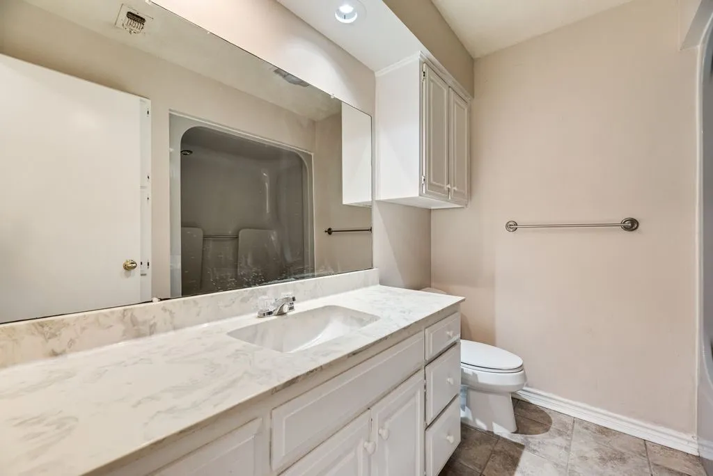Bathroom featuring a white vanity with an integrated sink, a large wall-mounted mirror, overhead recessed lighting, and a white toilet