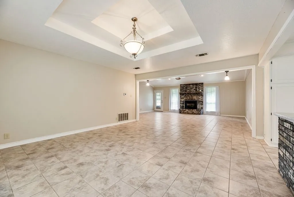 Expansive tiled flooring spans the open concept room, featuring a tray ceiling with a central chandelier