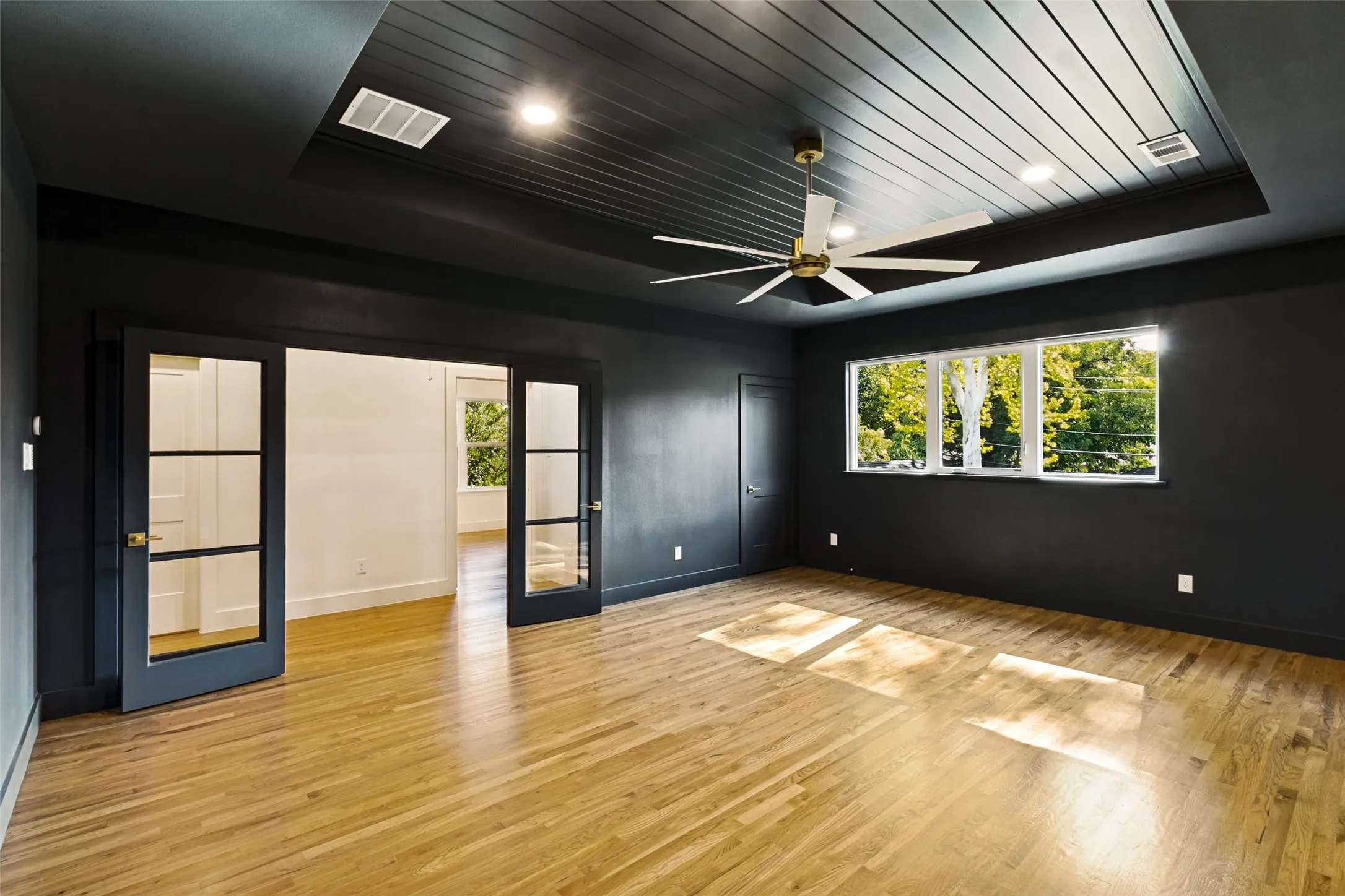 Spacious room featuring wood-finish flooring, a tray ceiling with recessed lighting, and a multi-pane window