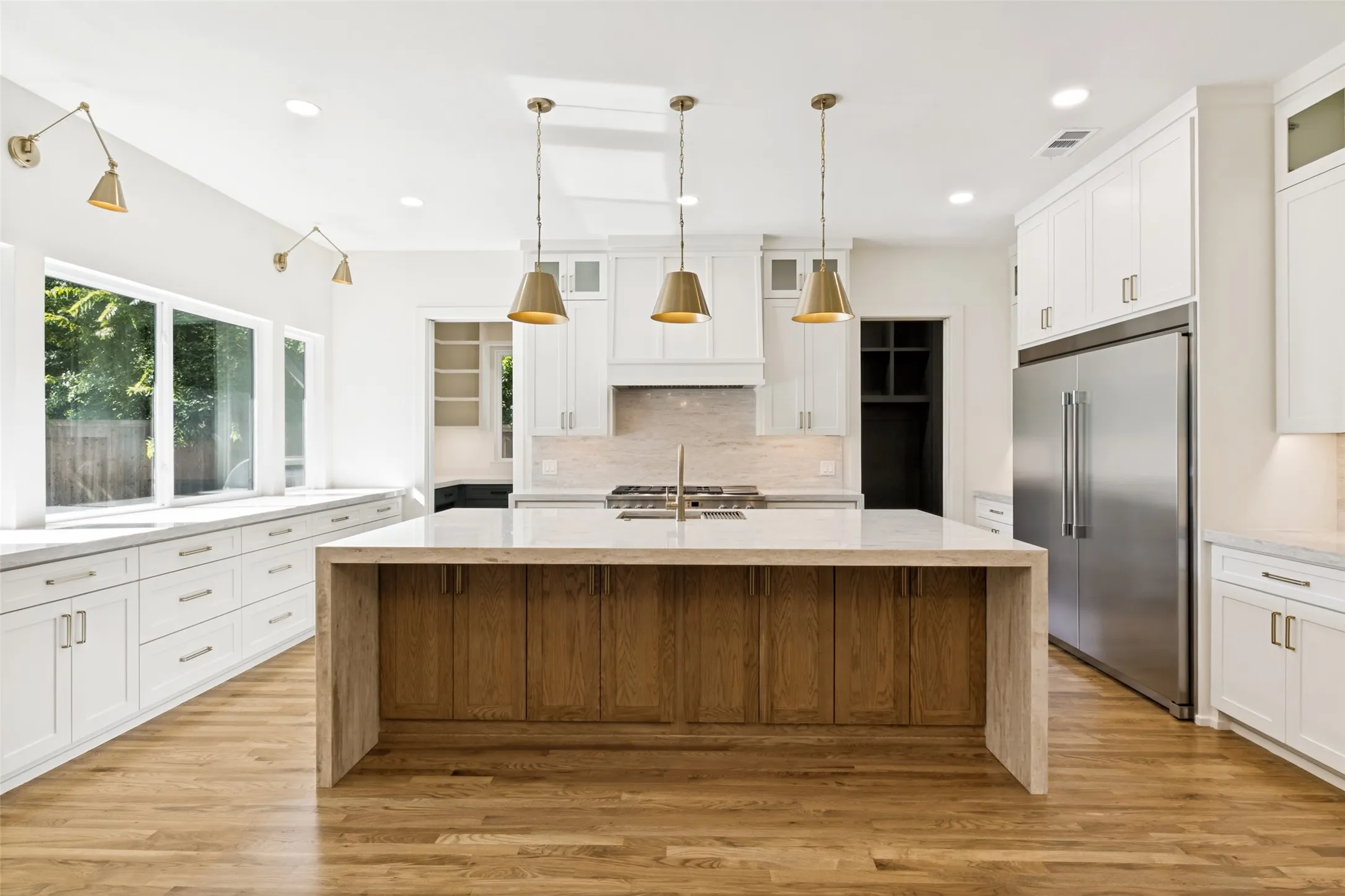 Kitchen featuring a waterfall island with wood-finish cabinetry, stainless steel appliances, recessed lighting, brass-toned pendant lights, and a window seat with built-in storage