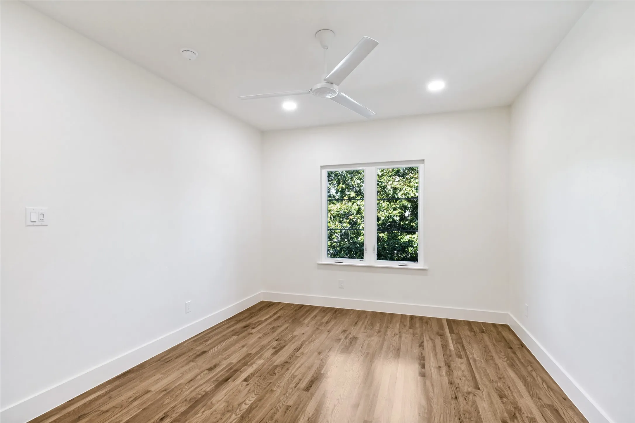 Bright room with wood-finish flooring, white walls, a multi-pane window, modern ceiling fan, and recessed lighting