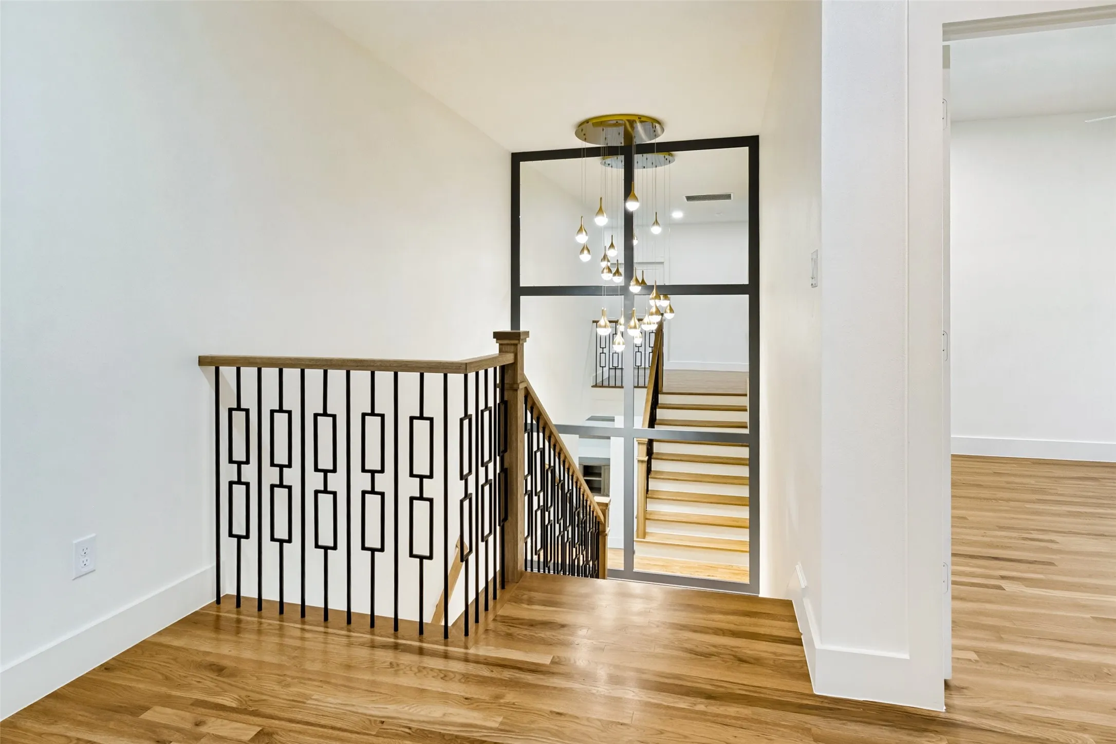 Stairwell featuring custom metal balusters, natural wood handrail, and wood-finish flooring