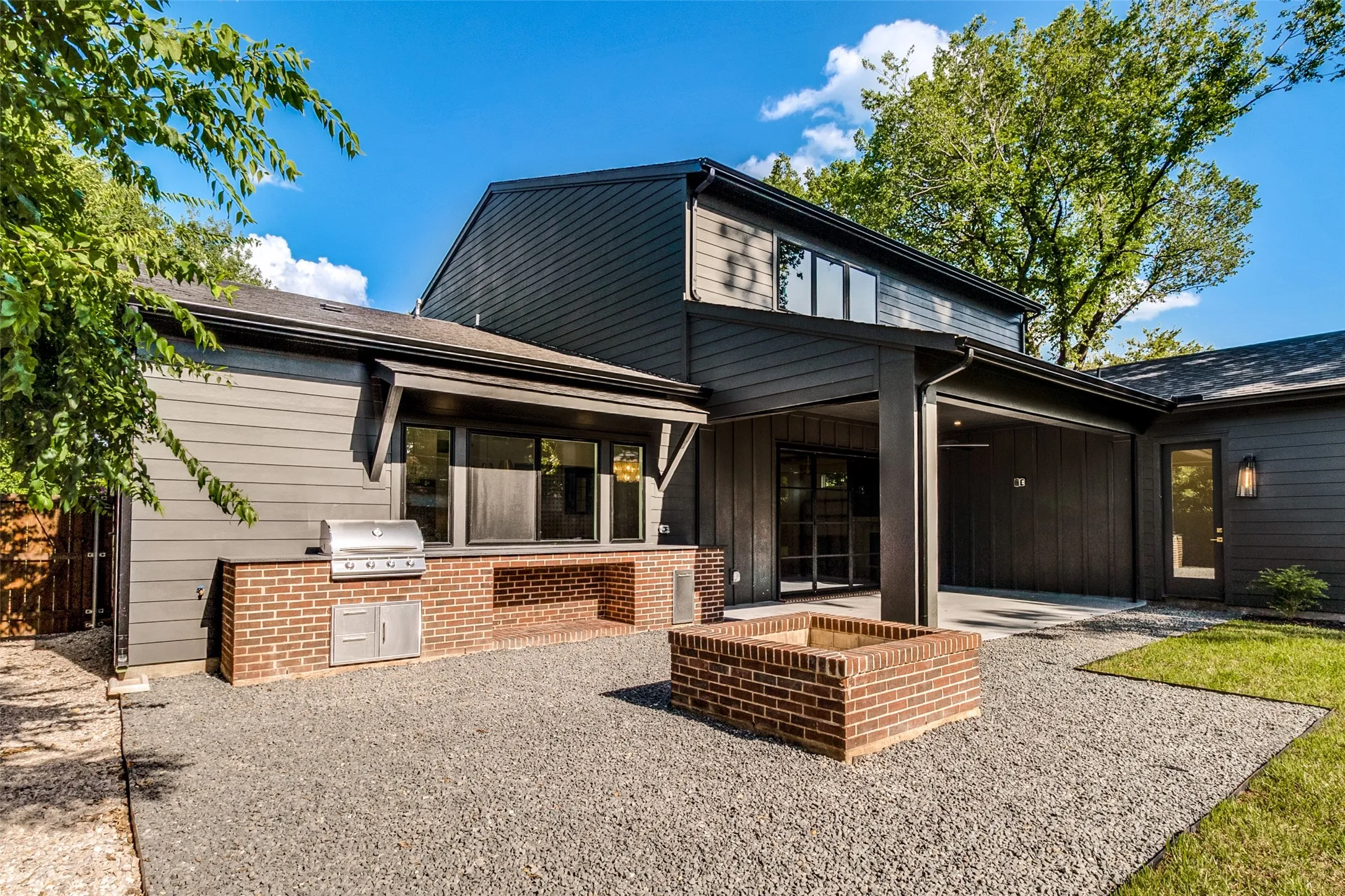 Exterior featuring dark-toned siding, a built-in brick fire pit, a built-in brick grilling station with stainless steel appliances, a covered patio, and large windows