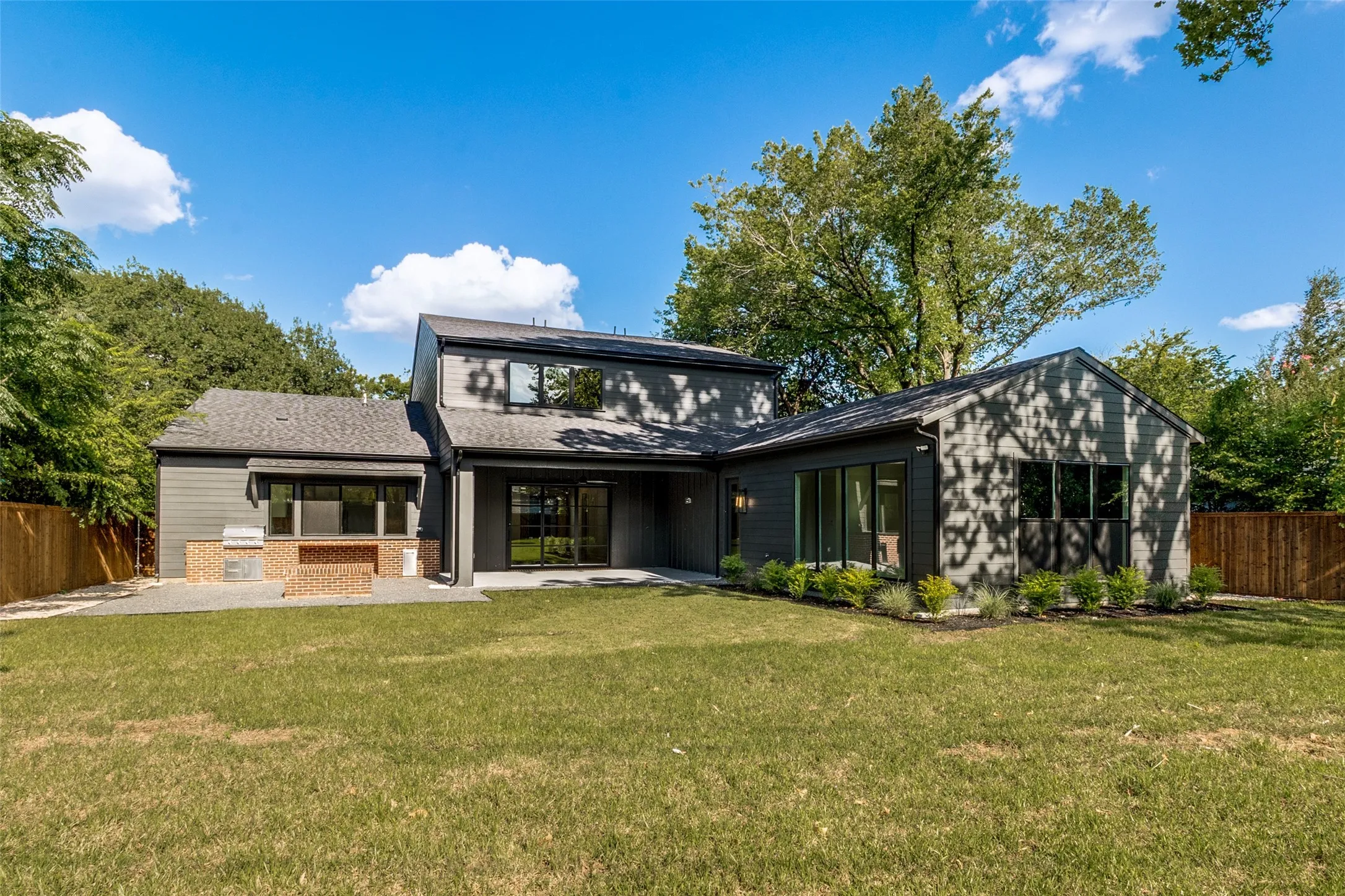 Expansive backyard featuring a manicured lawn, a large patio space, and a built-in outdoor kitchen with brick-finish accents