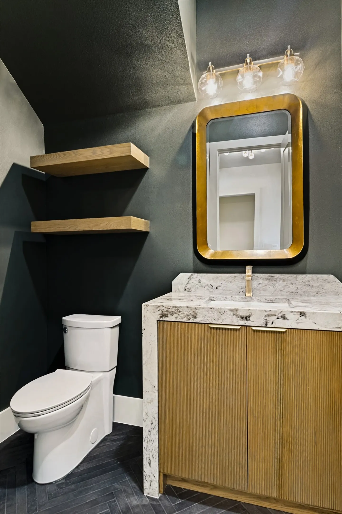 Bathroom featuring a wood-finish vanity with a stone countertop, a gold-framed mirror, and a three-light vanity fixture