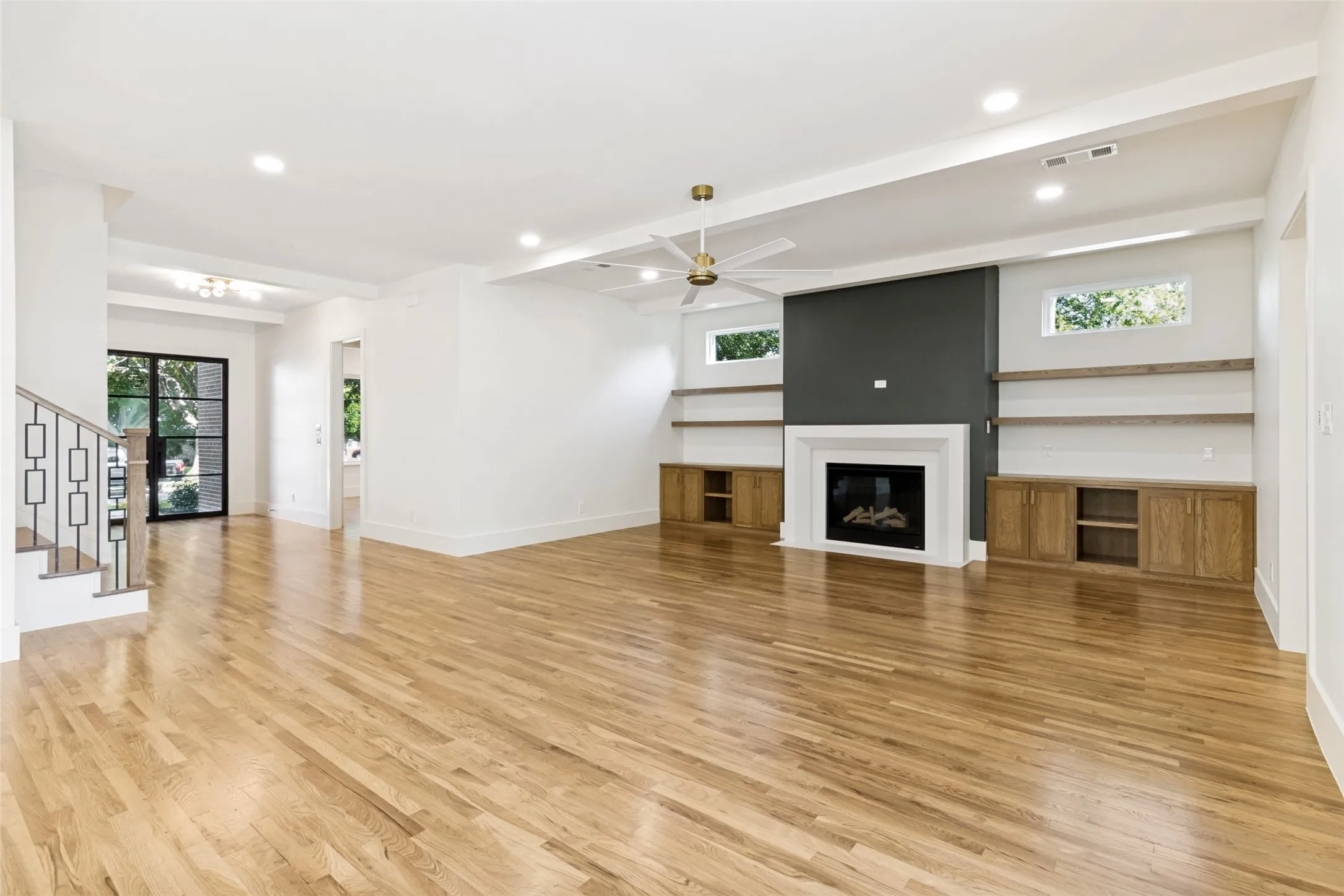Spacious room featuring wood-finish flooring, a contemporary fireplace with a dark accent wall, built-in cabinetry, floating shelves, and a ceiling fan with integrated lighting