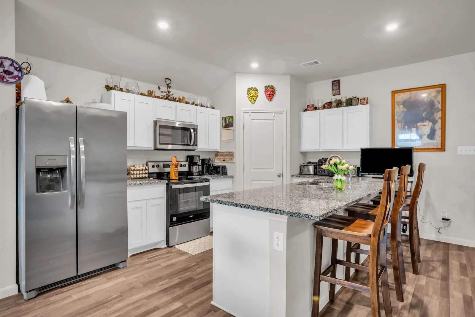 Kitchen featuring white cabinetry, stainless steel appliances, speckled stone countertops, a central island with integrated sink, and wood-finish flooring