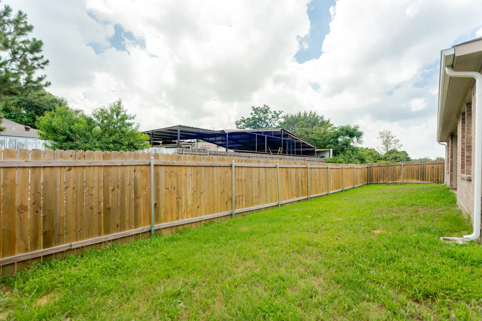 Expansive fenced backyard featuring a grassy lawn, a wood plank privacy fence, and a brick exterior building wall with gutters