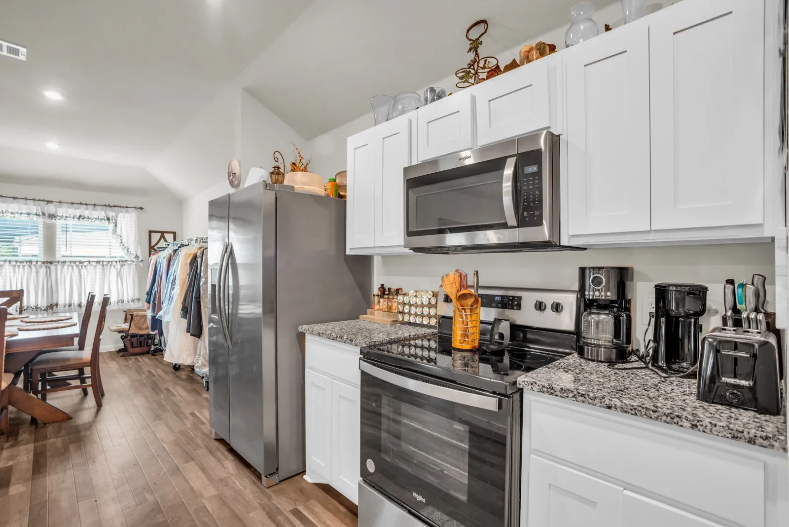 Kitchen featuring white shaker-style cabinetry, granite-finish countertops, and stainless steel appliances including a range with an overhead microwave
