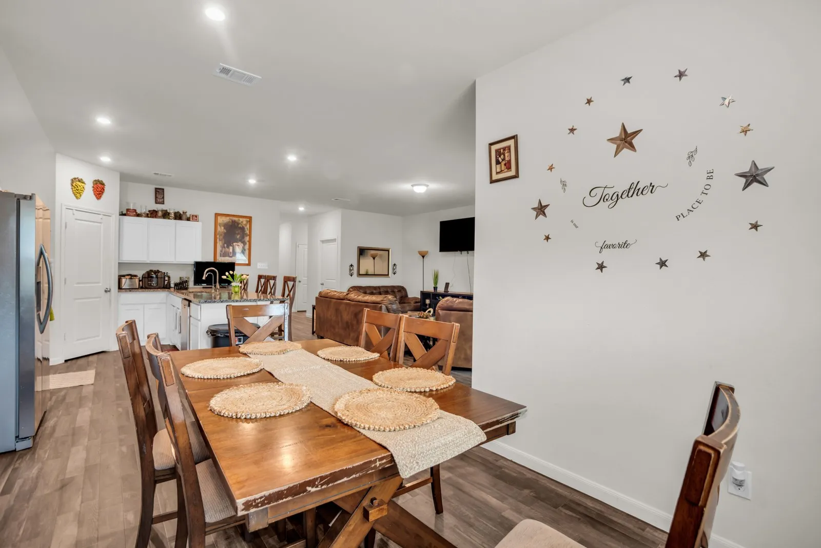 Open-concept dining and kitchen area featuring wood-finish flooring, recessed lighting, white cabinetry, and an island with bar seating