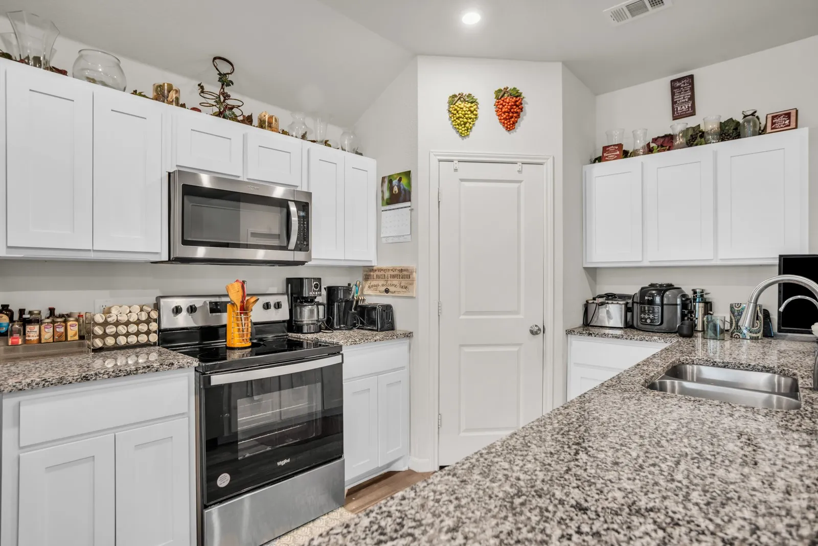Kitchen featuring white shaker-style cabinetry, speckled countertops, stainless steel appliances, and a stainless steel double-basin sink with a gooseneck faucet