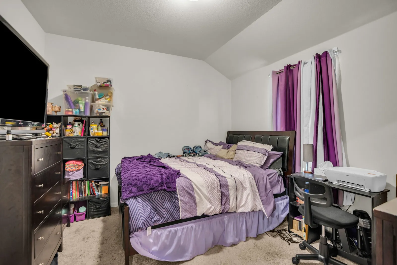 Carpeted room with a vaulted ceiling, featuring a window with curtain rod, and neutral wall tones