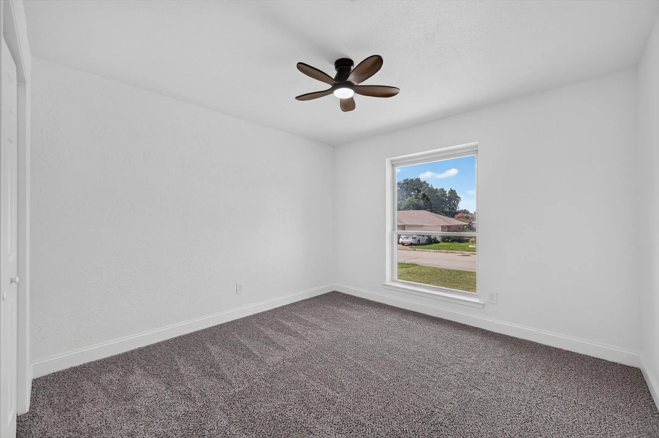 Spacious room featuring neutral carpeting, white wall finishes, and a single window offering exterior views