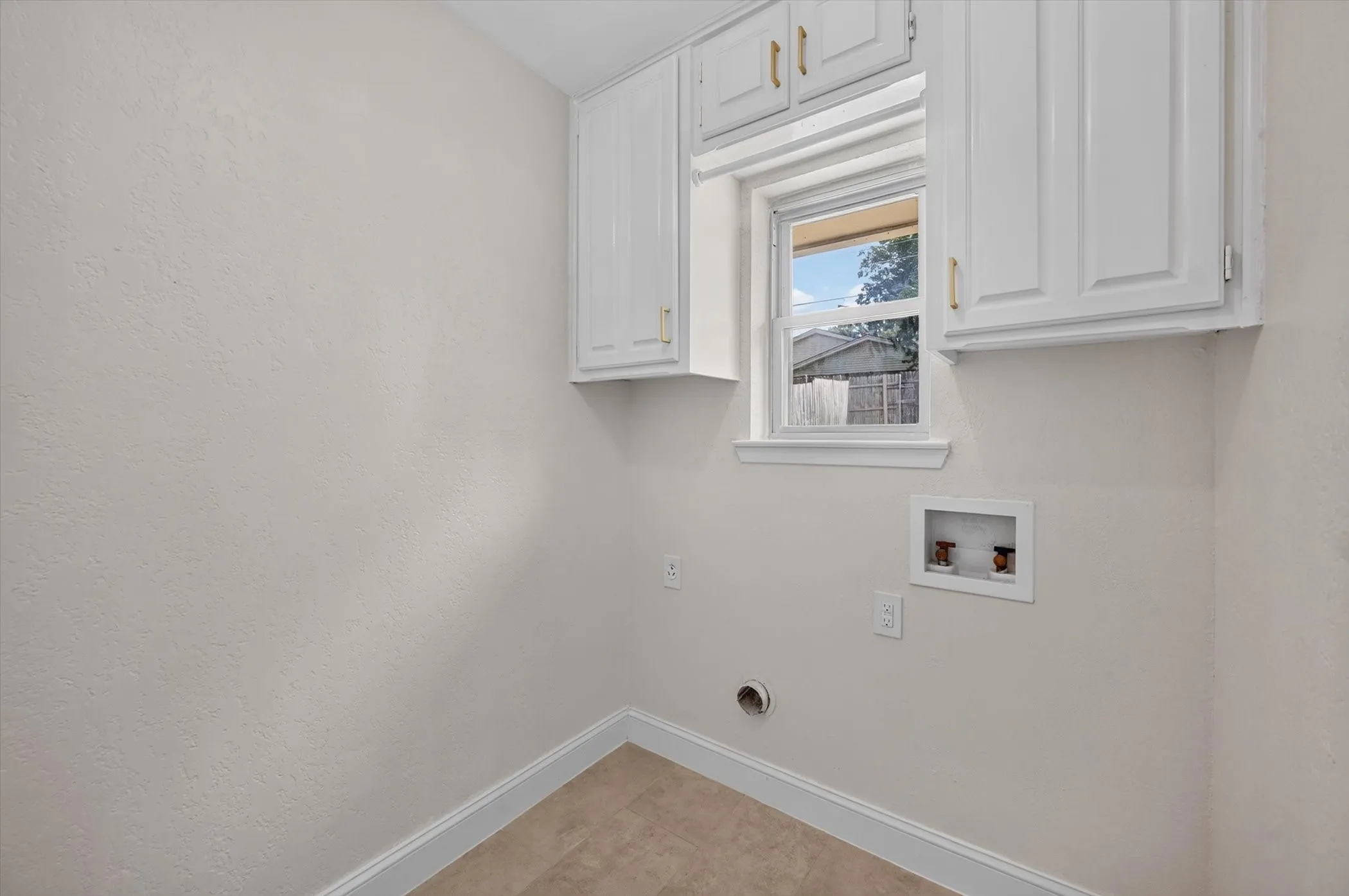 Dedicated utility space featuring white upper cabinetry, a window, and durable tile flooring