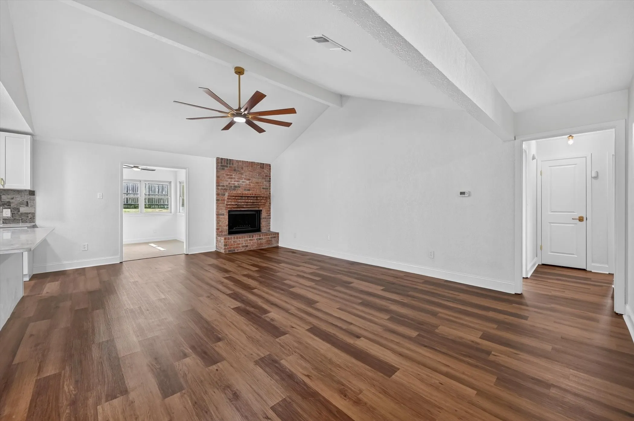 Spacious living area featuring vaulted ceilings, a brick-surround fireplace, wood-finish flooring, and a contemporary ceiling fan