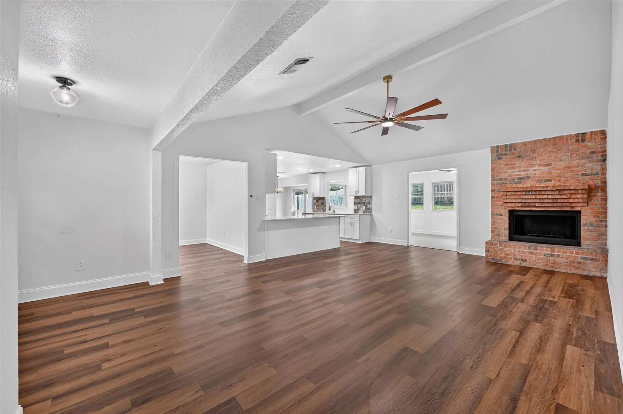 Spacious living area featuring wood-finish flooring, a brick fireplace, a vaulted ceiling, and a large ceiling fan