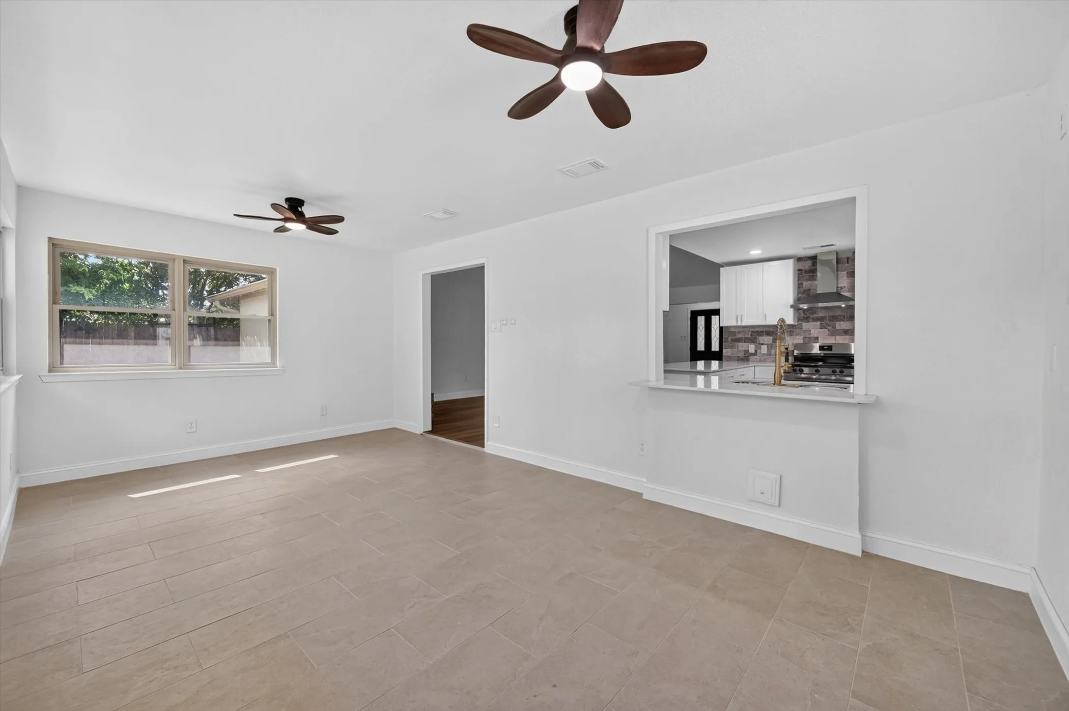 Bright living space featuring large format tile flooring, white painted walls, and two ceiling fans