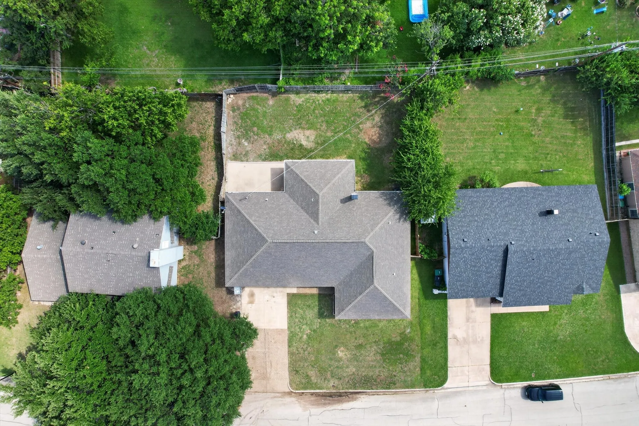 Gable roofline residence with a driveway, mature trees, and an expansive grassy yard