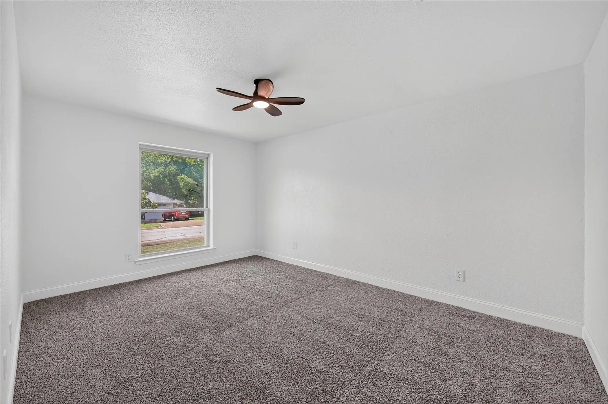 Spacious room featuring neutral carpeting, white walls, a large window, white trim, and a ceiling fan with integrated lighting