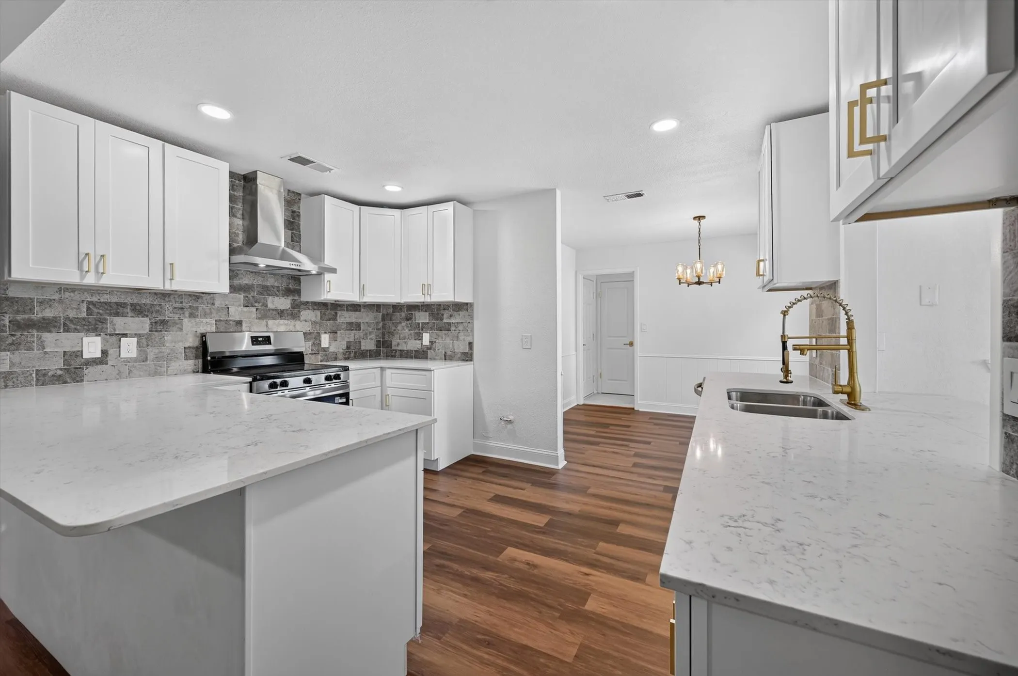 Modern kitchen featuring white cabinetry, light-colored countertops, a stainless steel range with a matching range hood, and a gray tile backsplash