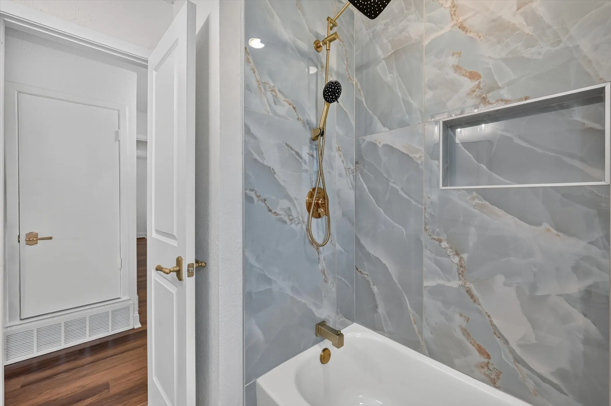 Bathroom featuring a bathtub with a gold-finish faucet and showerhead, marble-look wall tiling, and a recessed shower niche