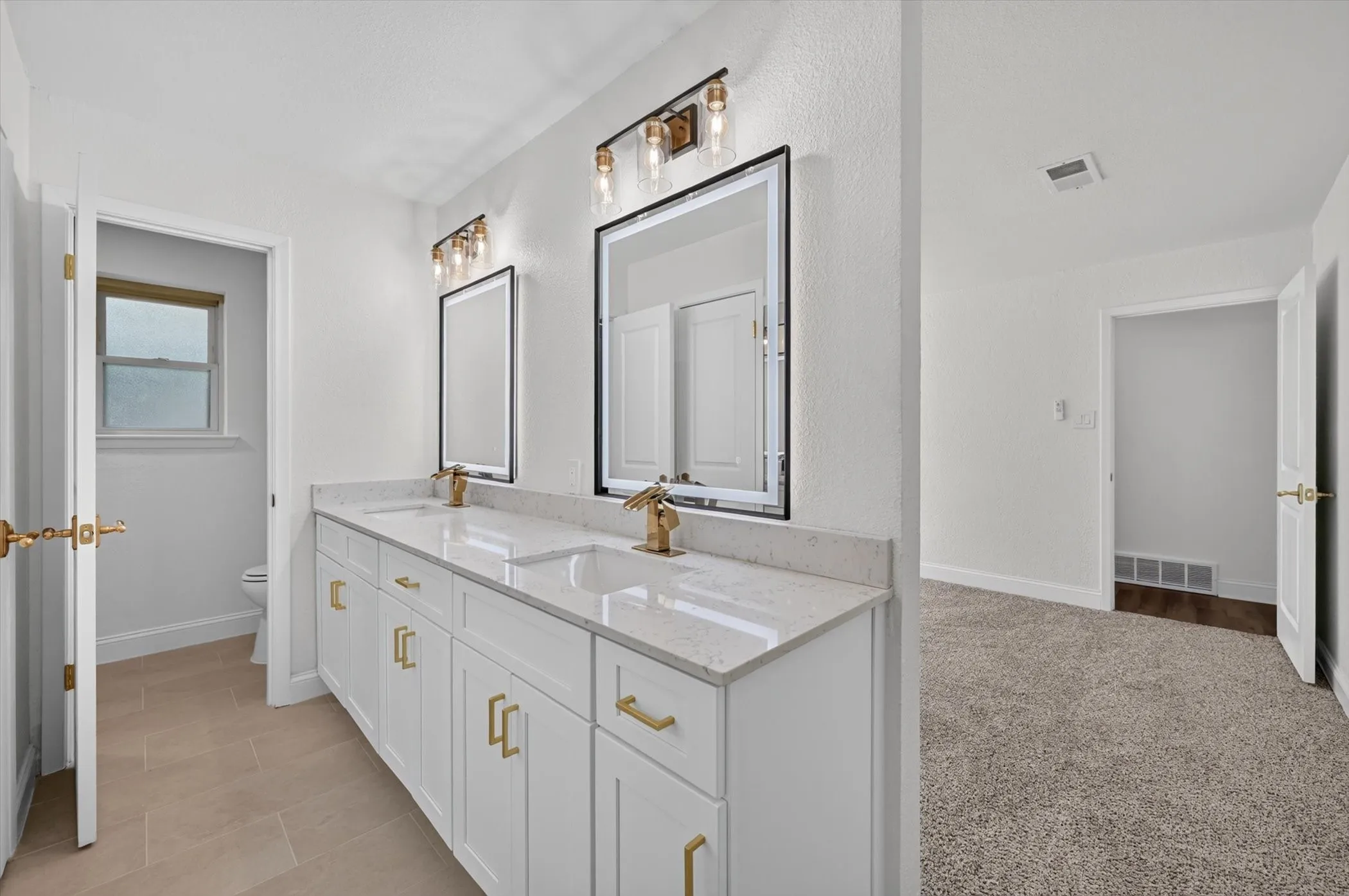 Dual vanity featuring white cabinetry, gold hardware, quartz countertops, and gold-finish faucets