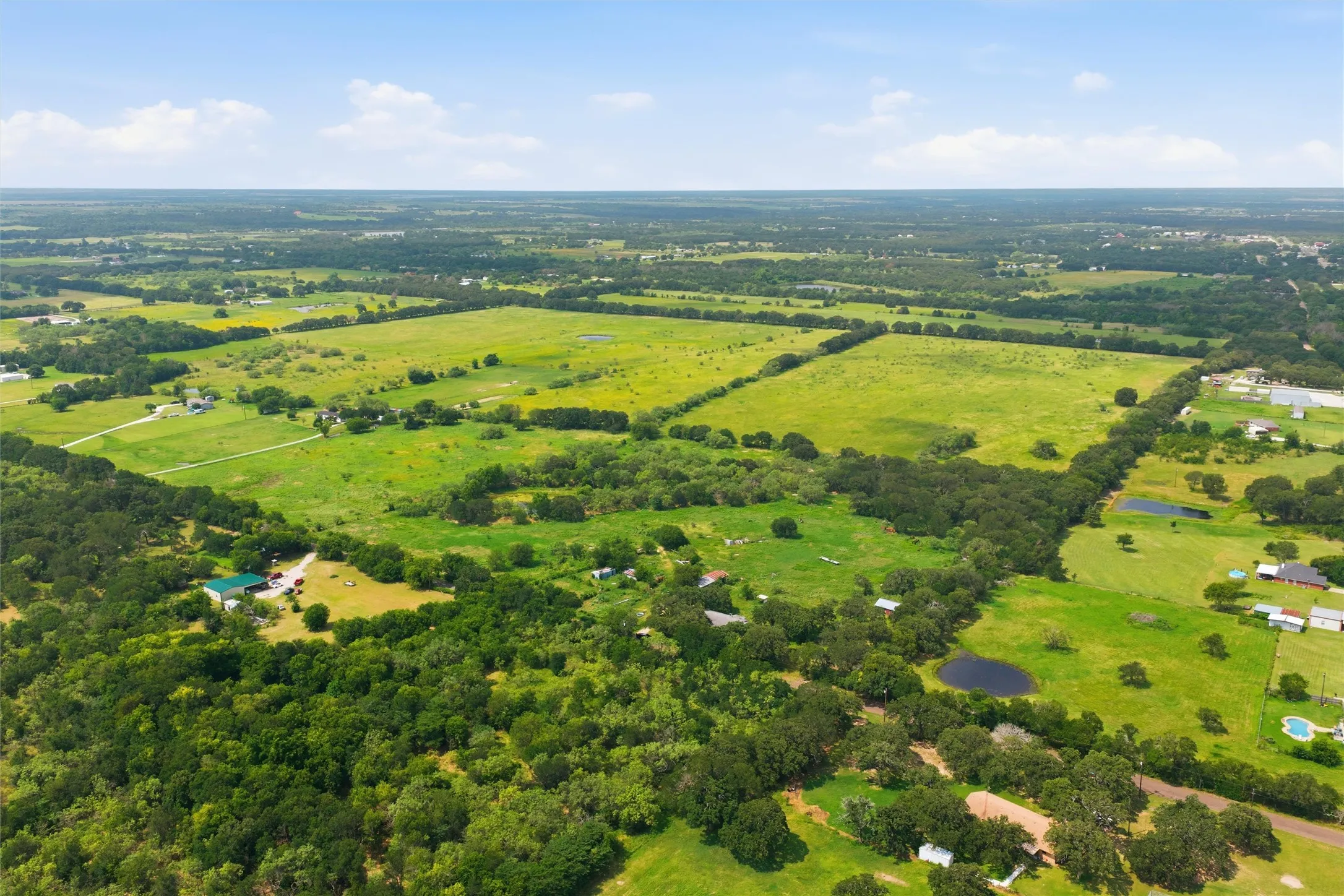 Expansive rural acreage featuring multiple clearings, mature tree lines, and a visible pond