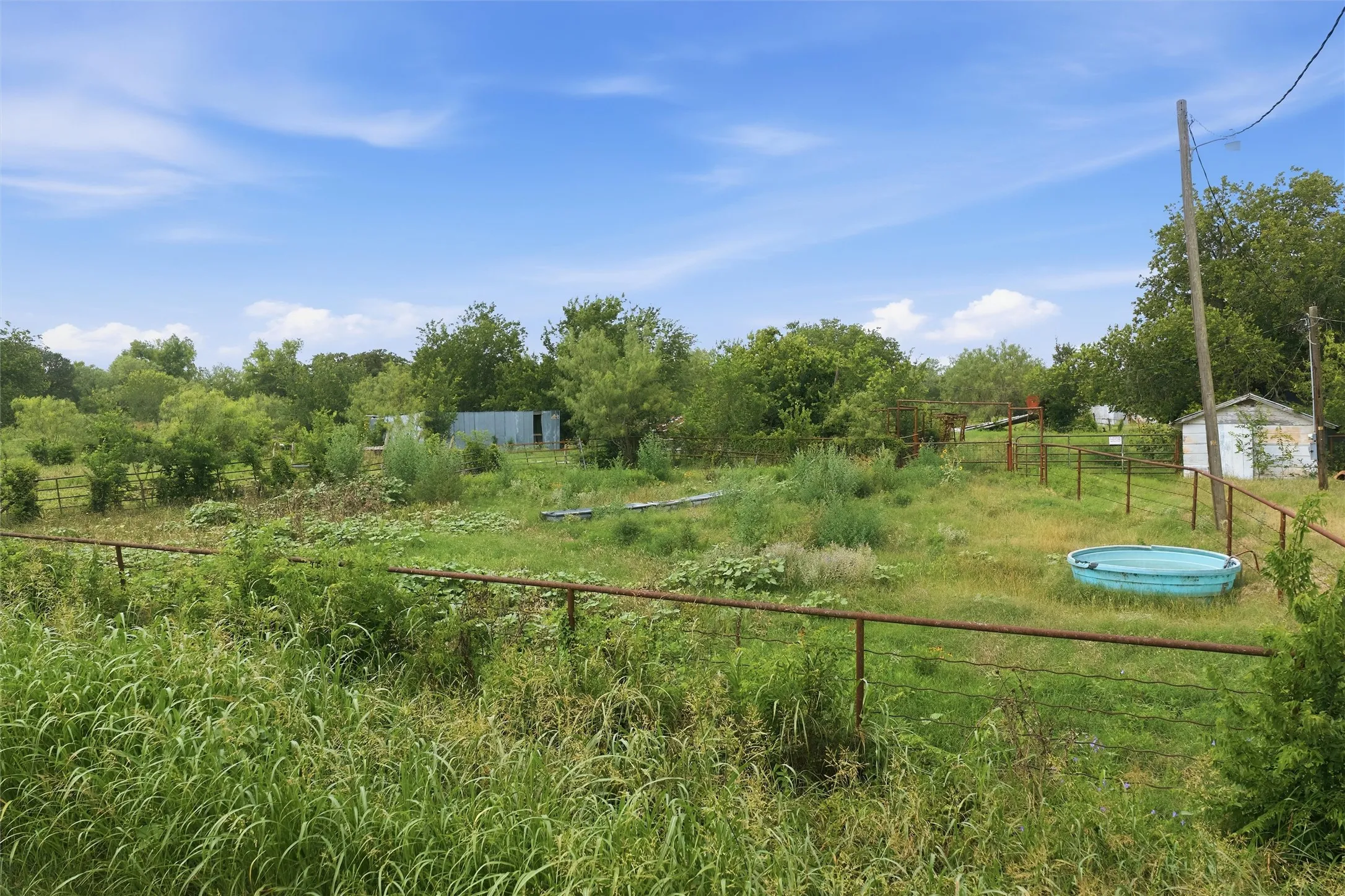 Expansive grassy acreage featuring perimeter fencing and a storage shed