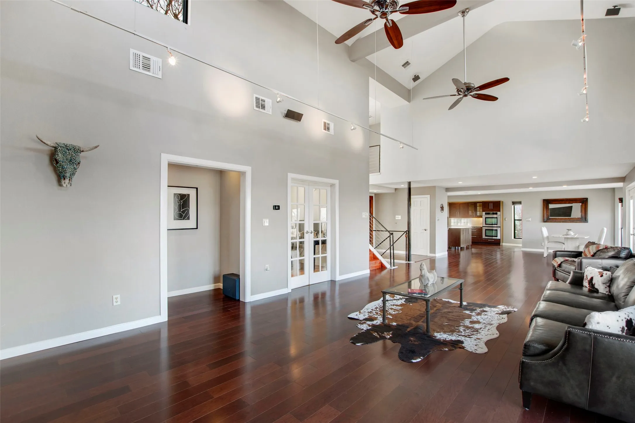 Spacious living area featuring high vaulted ceilings, multiple ceiling fans, dark wood-finish flooring, and white trim