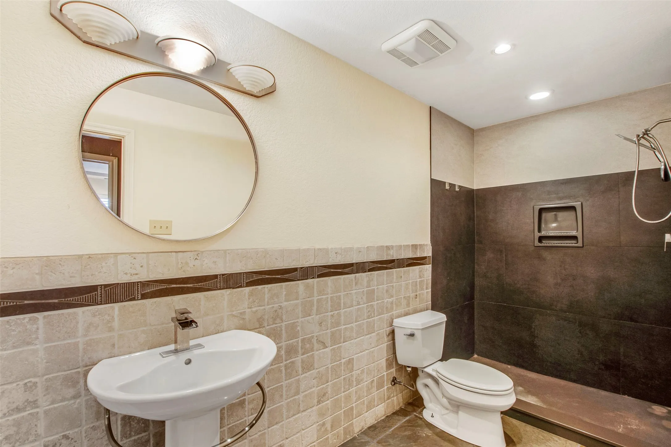 Bathroom featuring a pedestal sink with a contemporary faucet, round wall-mounted mirror, and vanity lighting
