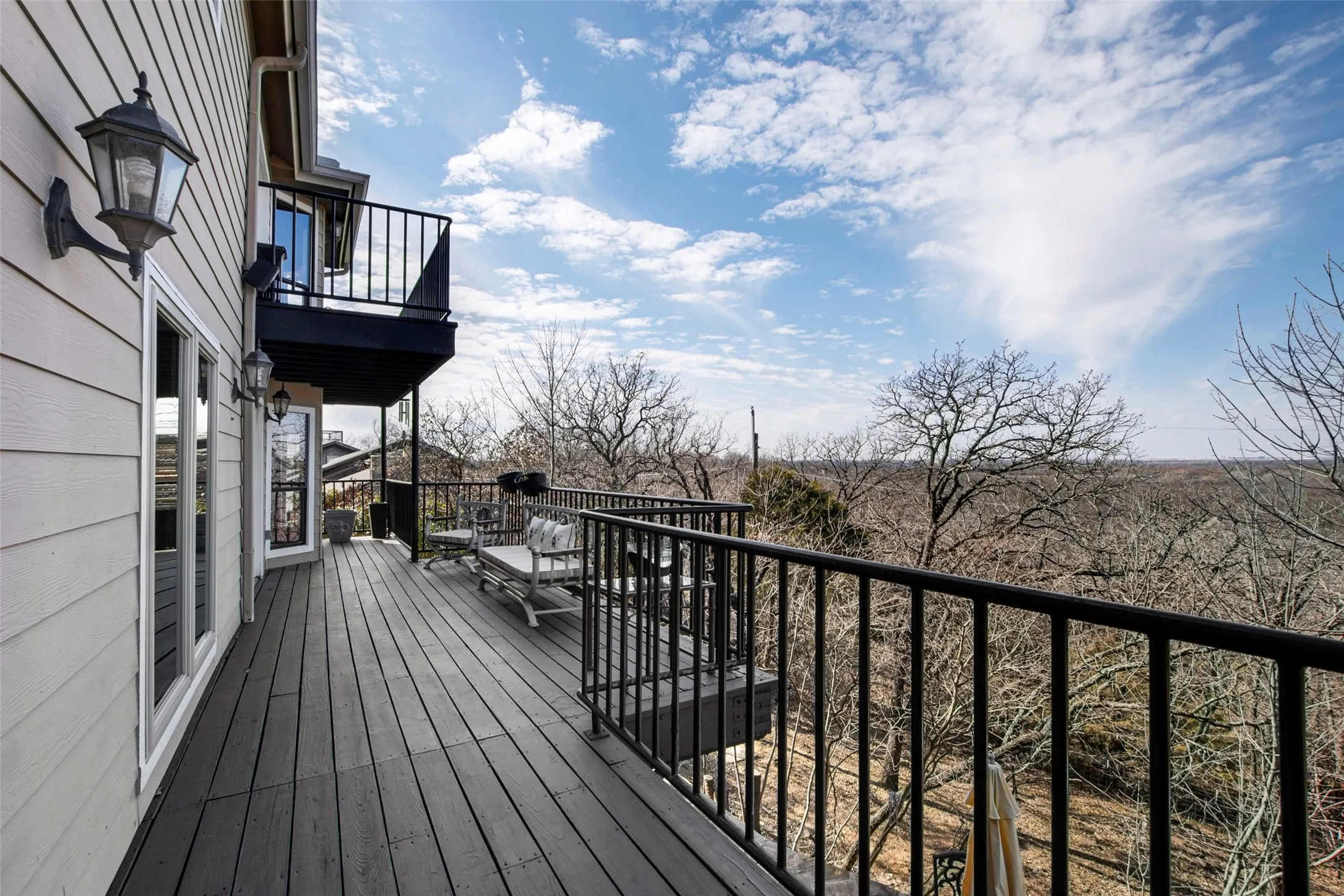 Spacious outdoor deck featuring gray wood-finish flooring, black metal railings, and a secondary upper balcony