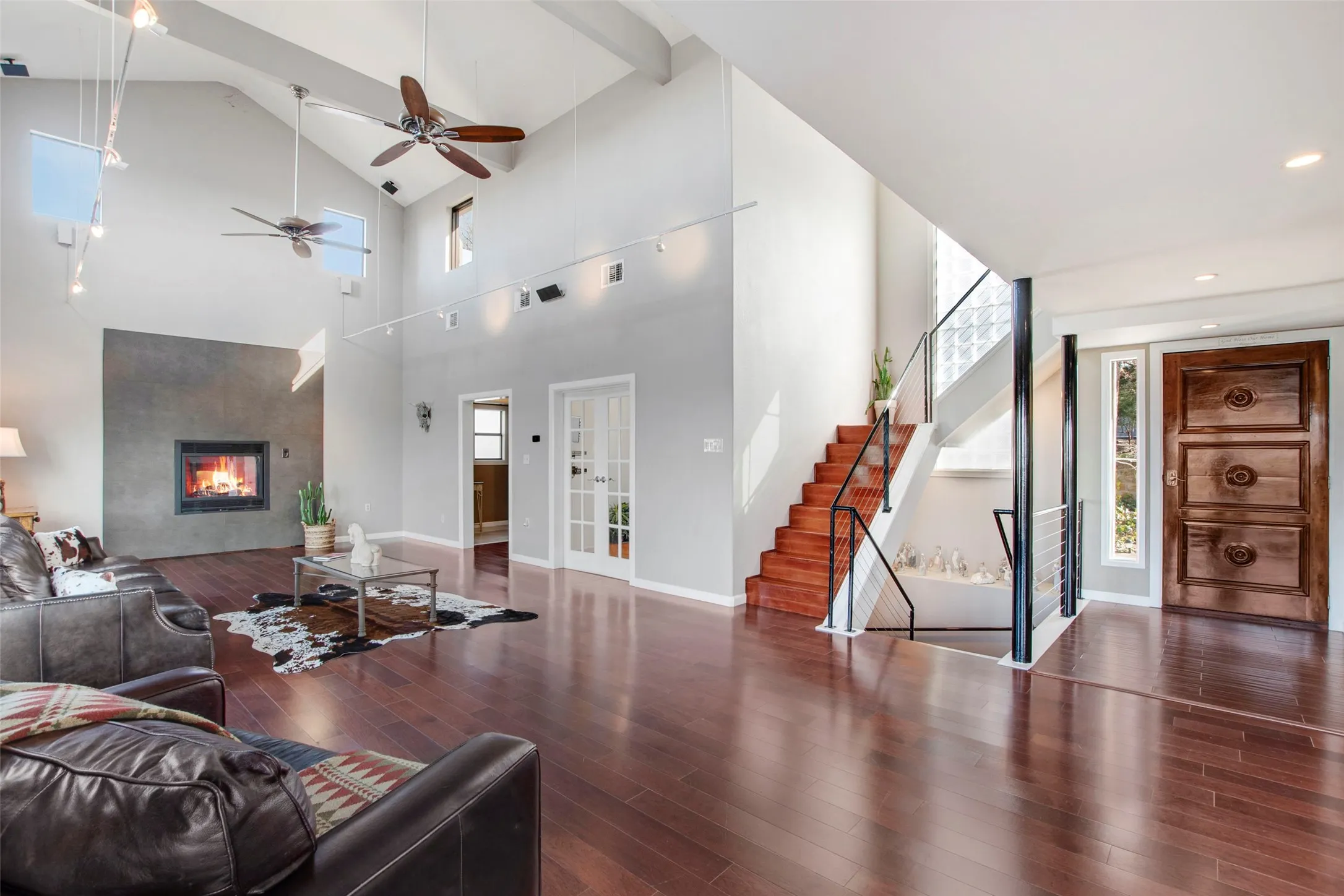 Vaulted ceiling living area featuring wood-finish flooring, a contemporary fireplace with a stone-finish surround, and a prominent staircase with metal railings