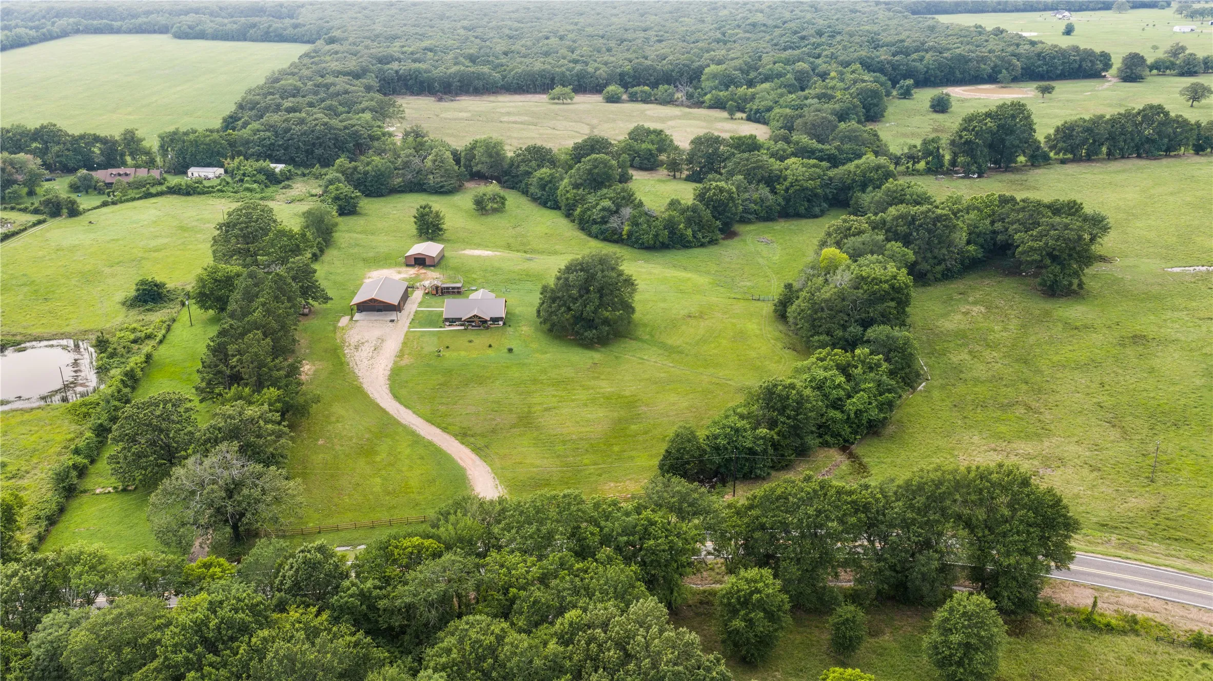 Expansive rural property featuring a main residence, additional outbuildings, a winding driveway, and a pond