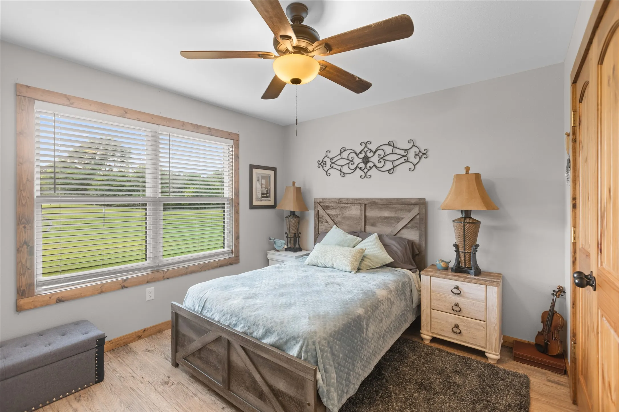 Hardwood-finish flooring throughout the room with a large window featuring natural wood trim and white blinds