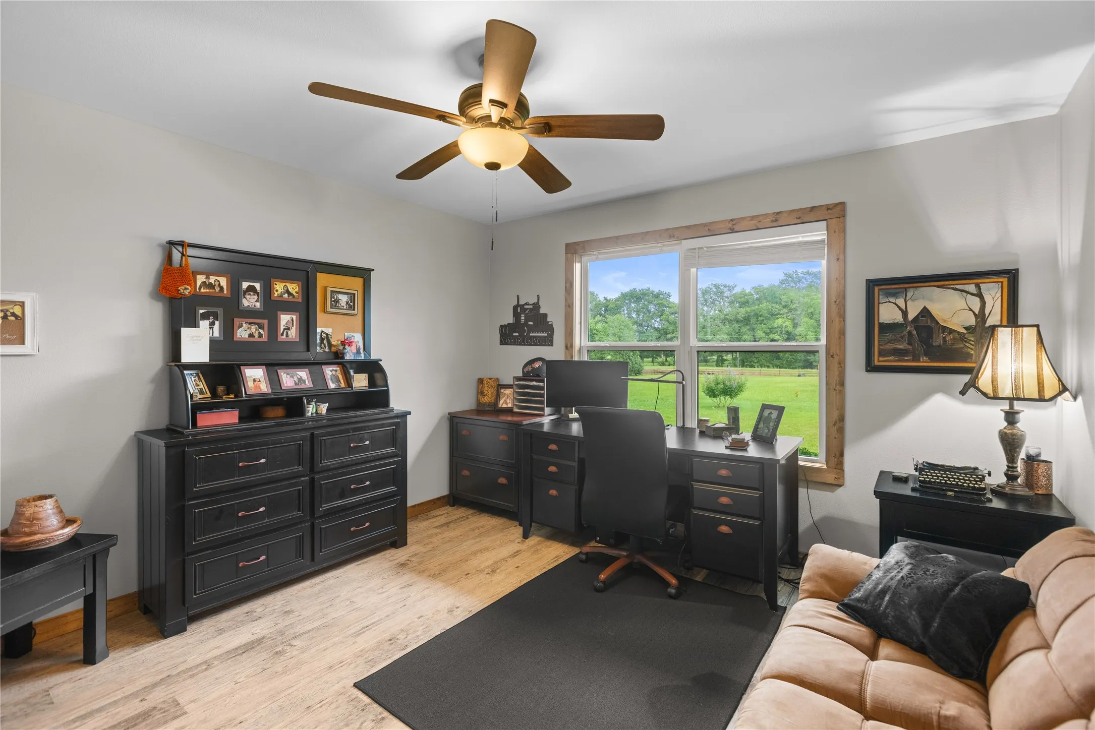 Room featuring wood-finish flooring, a ceiling fan with integrated lighting, and a large window with wood trim