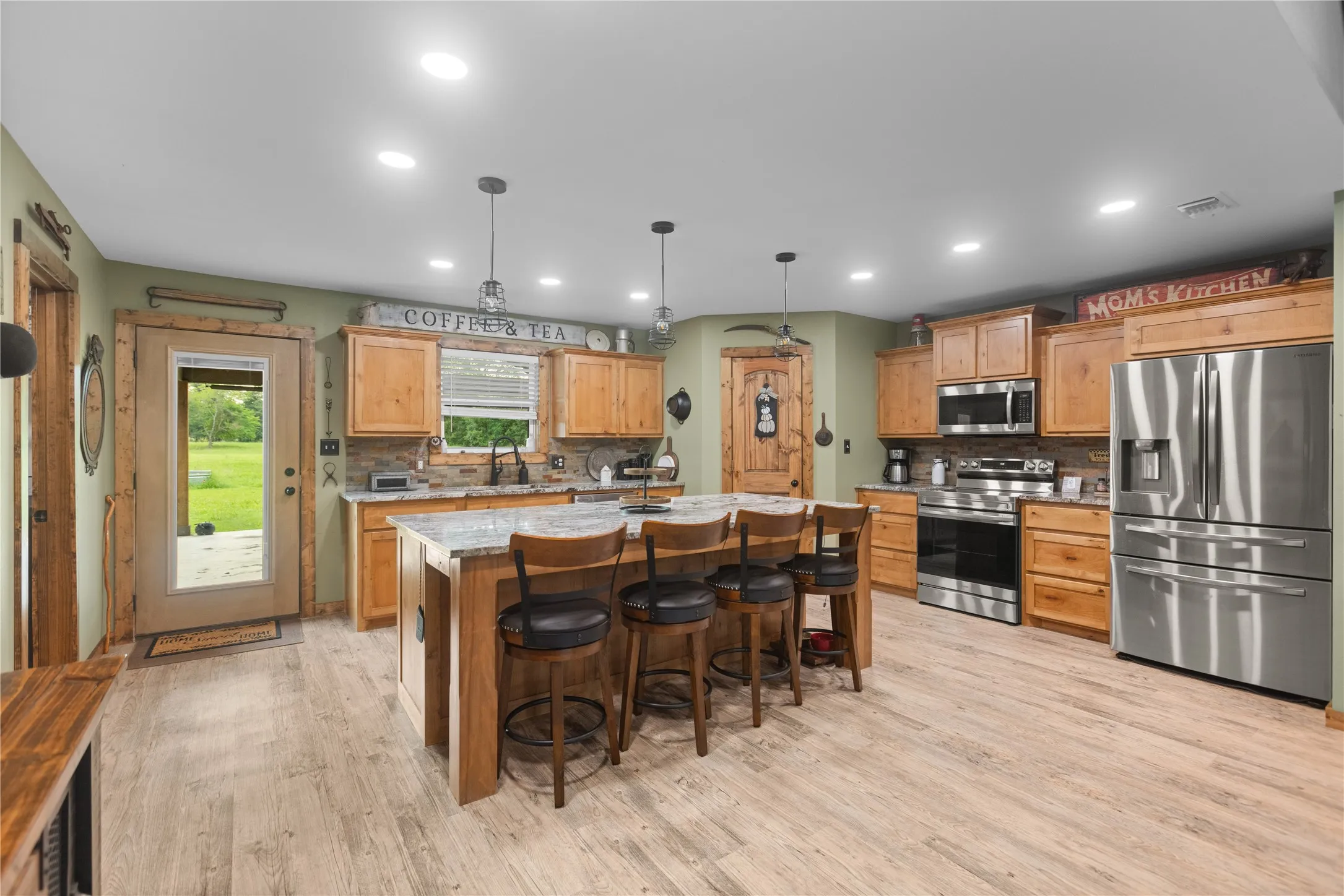 Spacious kitchen featuring a central island with seating, stainless steel appliances, wood-finish flooring, recessed lighting, and a glass-paned exterior door