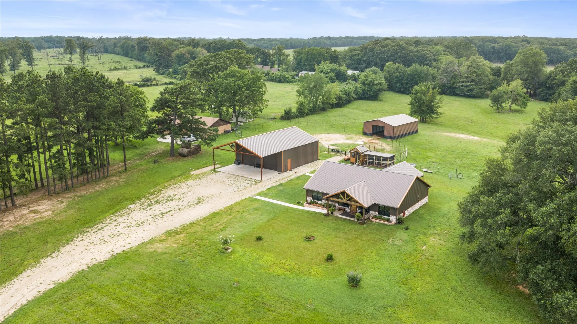 Expansive property featuring a brown ranch-style home with a metal roof, a detached carport, and a separate barn