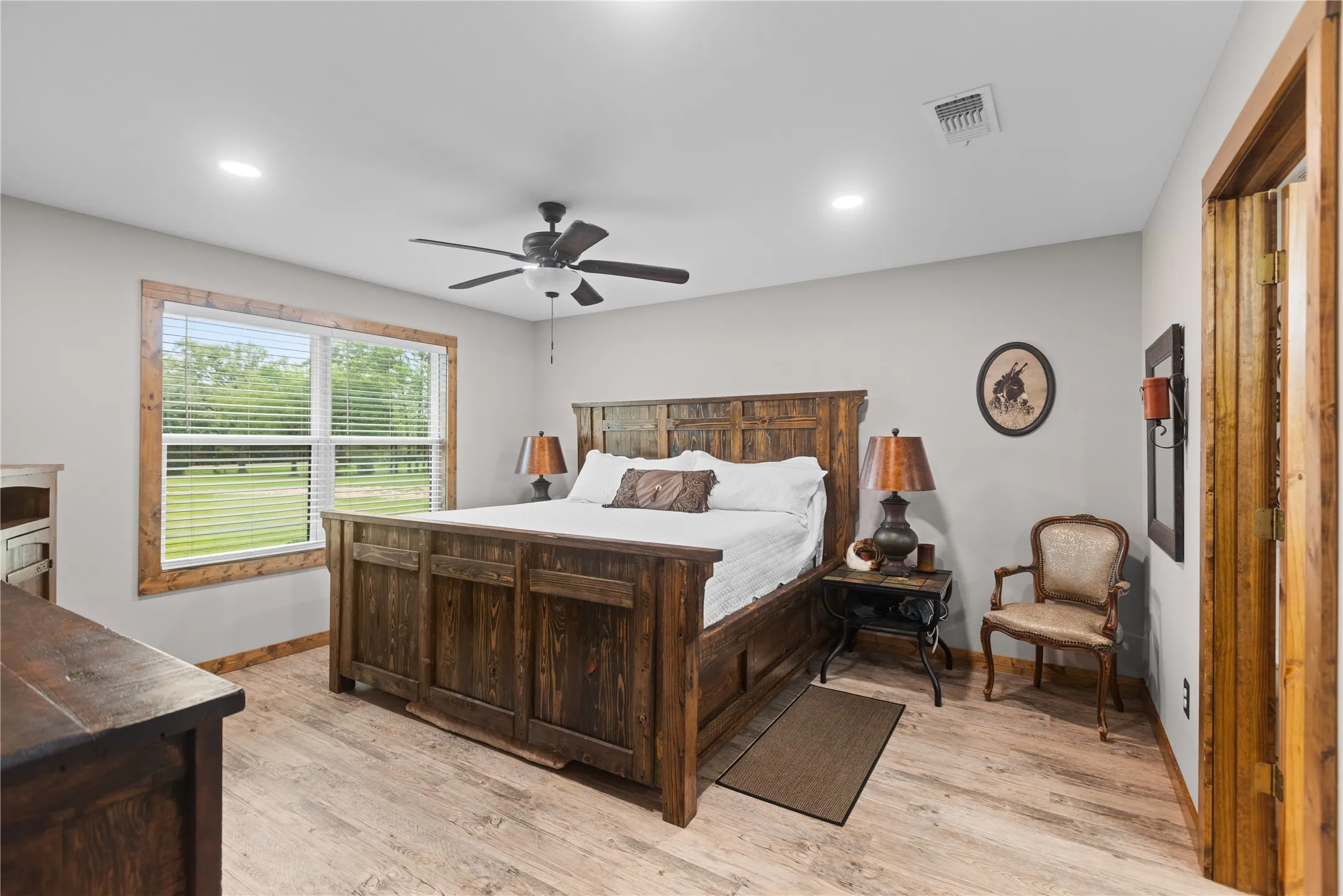 Spacious room featuring wood-finish flooring, light grey walls, and a large window with white blinds