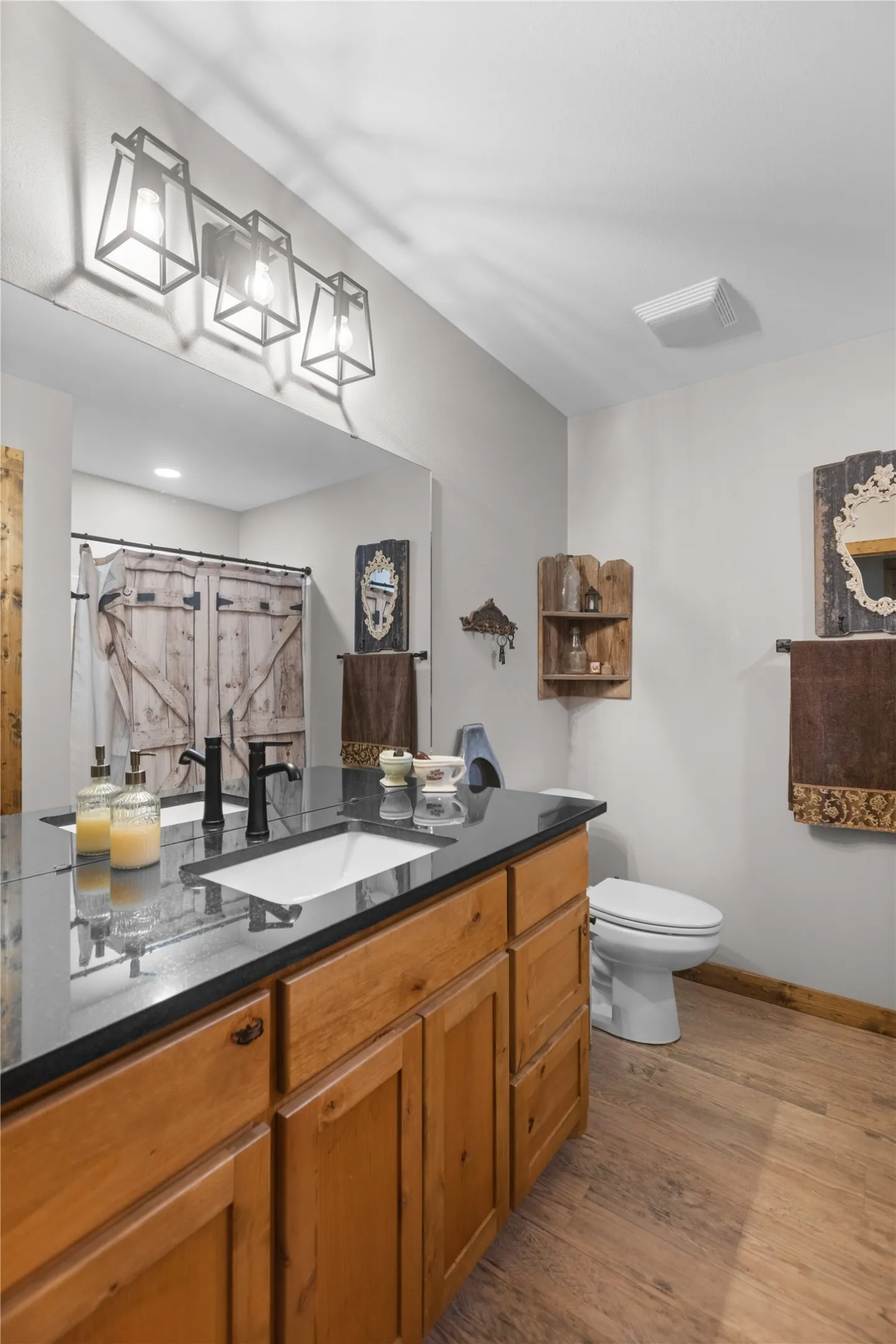 Double vanity with wood-finish cabinetry and a black countertop, featuring dual undermount sinks and matte black faucets